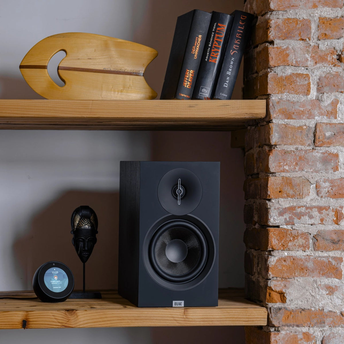 ELAC Debut B5.3 passive bookshelf speakers shown in a modern living room setting with wood finish and speaker grilles attached.