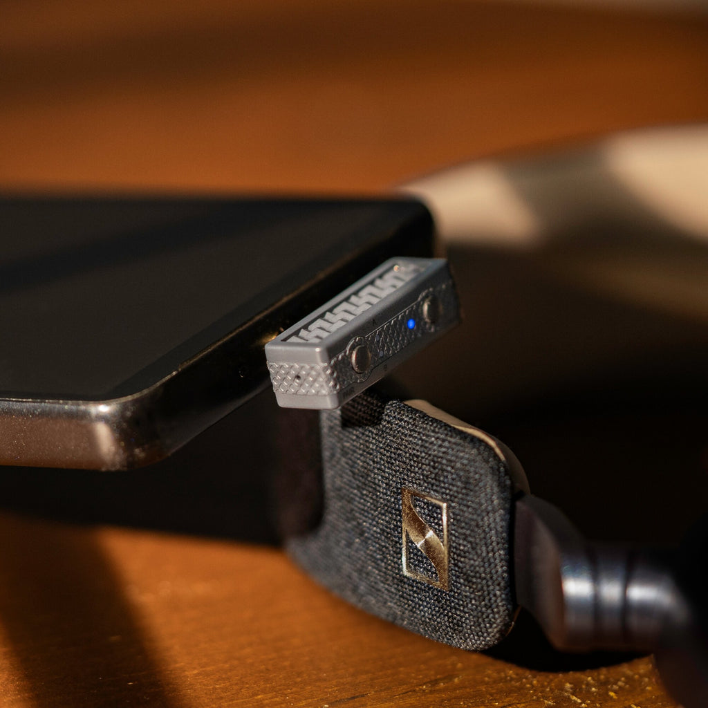 iFi Audio UP Play Max plugged into a smartphone beside wireless headphones